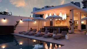 A modern outdoor pool area with lounge chairs and umbrellas, a bar, and a pool reflecting the sky. - Bali Hotel Adults Only Isla Verde, a Trademark by Wyndham (Carolina)