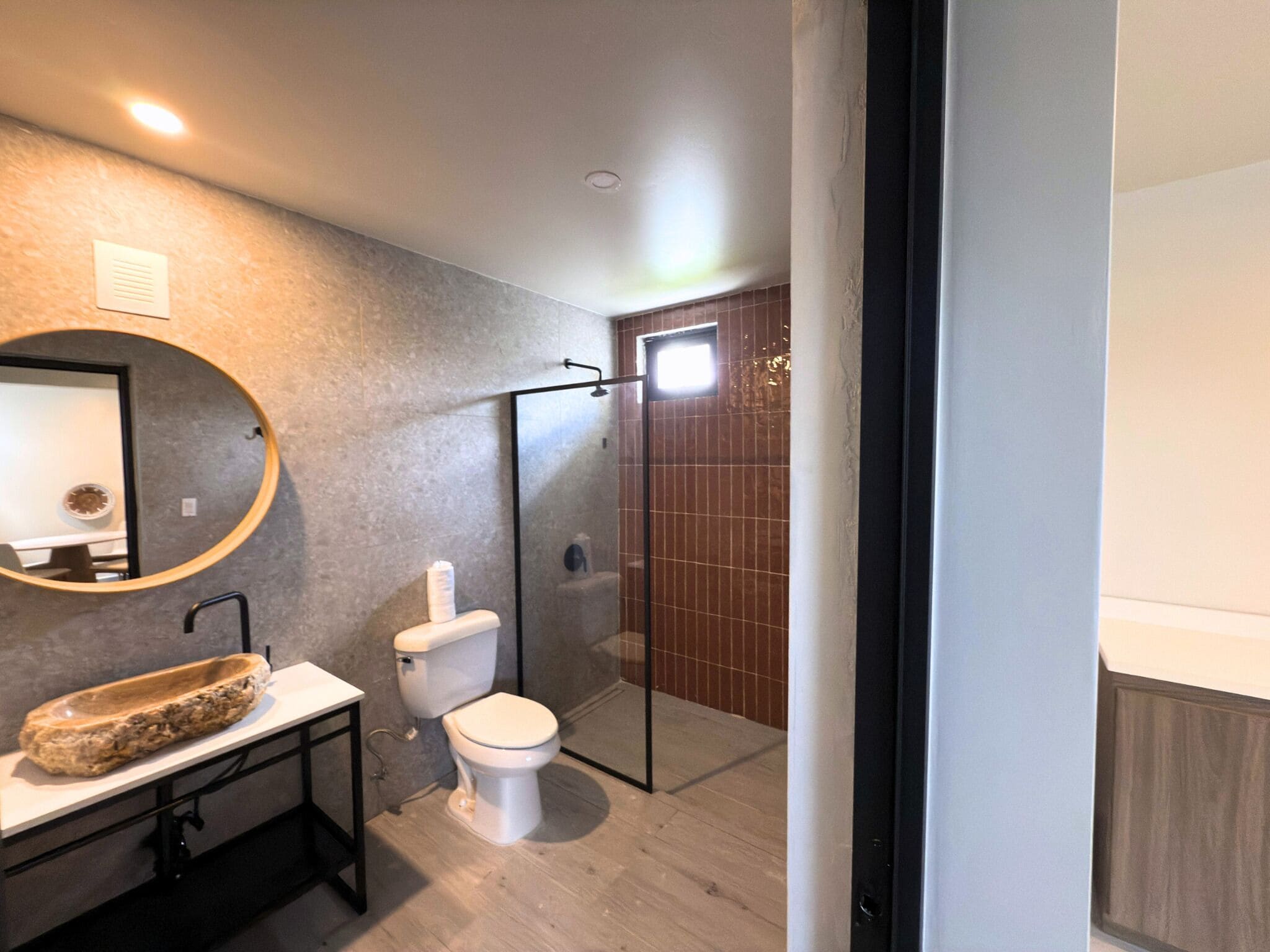 A modern bathroom with a round mirror, a sink with a stone basin, a toilet, and a glass-enclosed shower area.