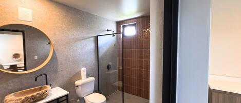 A modern bathroom with a round mirror, a sink with a stone basin, a toilet, and a glass-enclosed shower area.