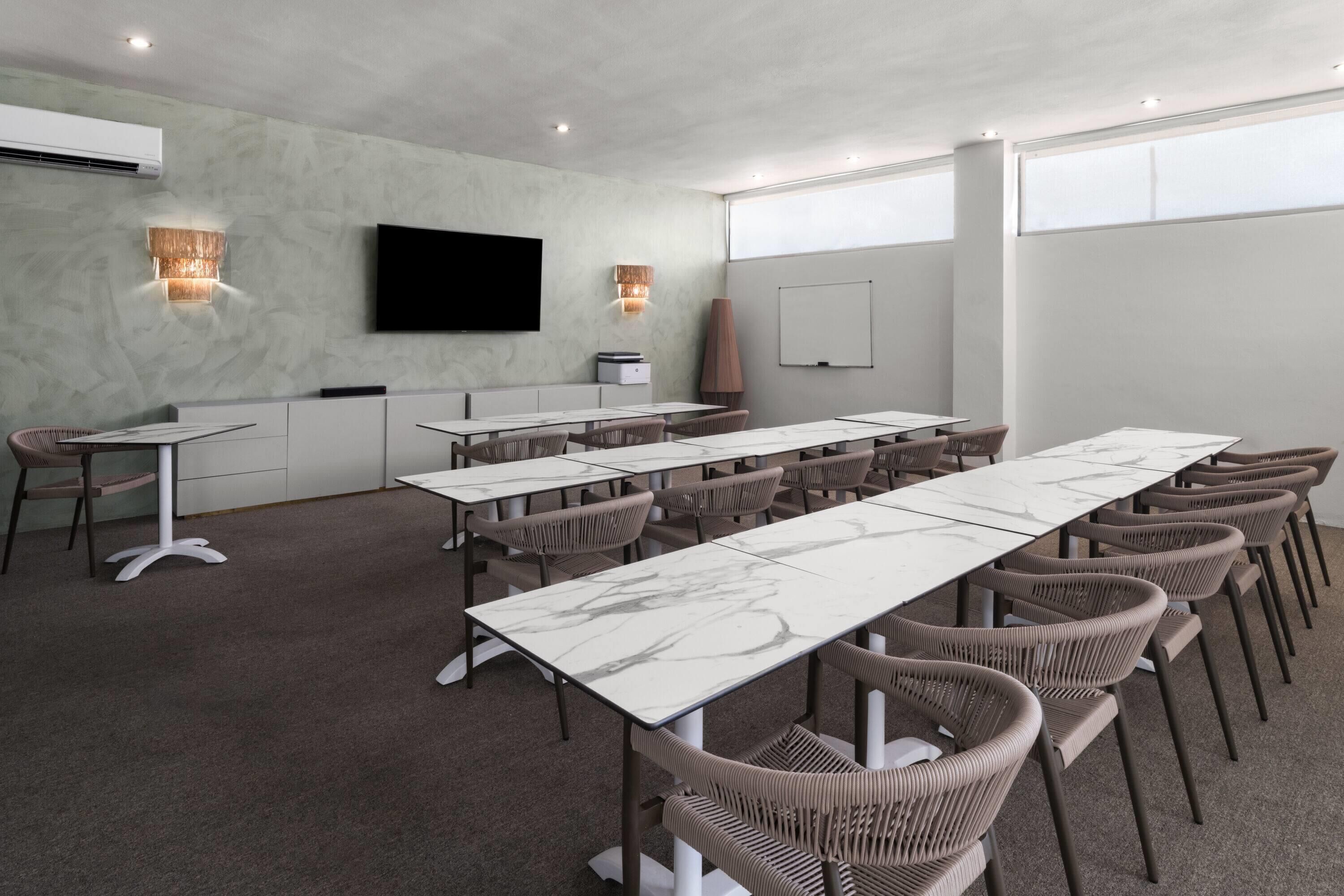 Un salón de conferencias con una larga mesa, sillas, un televisor y luces instaladas en la pared.
