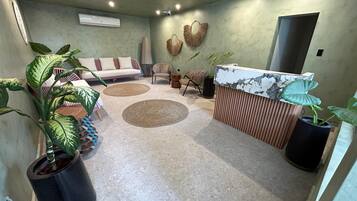 Habitación moderna y bien iluminada con sofá, sillas, mostrador de recepción y plantas en macetas.