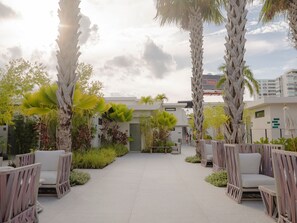 An outdoor patio area with seating and palm trees, leading to a building entrance. - Bali Hotel Adults Only Isla Verde, a Trademark by Wyndham (Carolina)