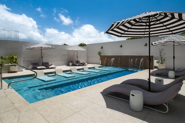 Una piscina con sillas de descanso y sombrillas a rayas.