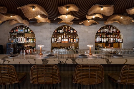 A bar area with a marble countertop, wicker chairs, and a ceiling with woven light fixtures.