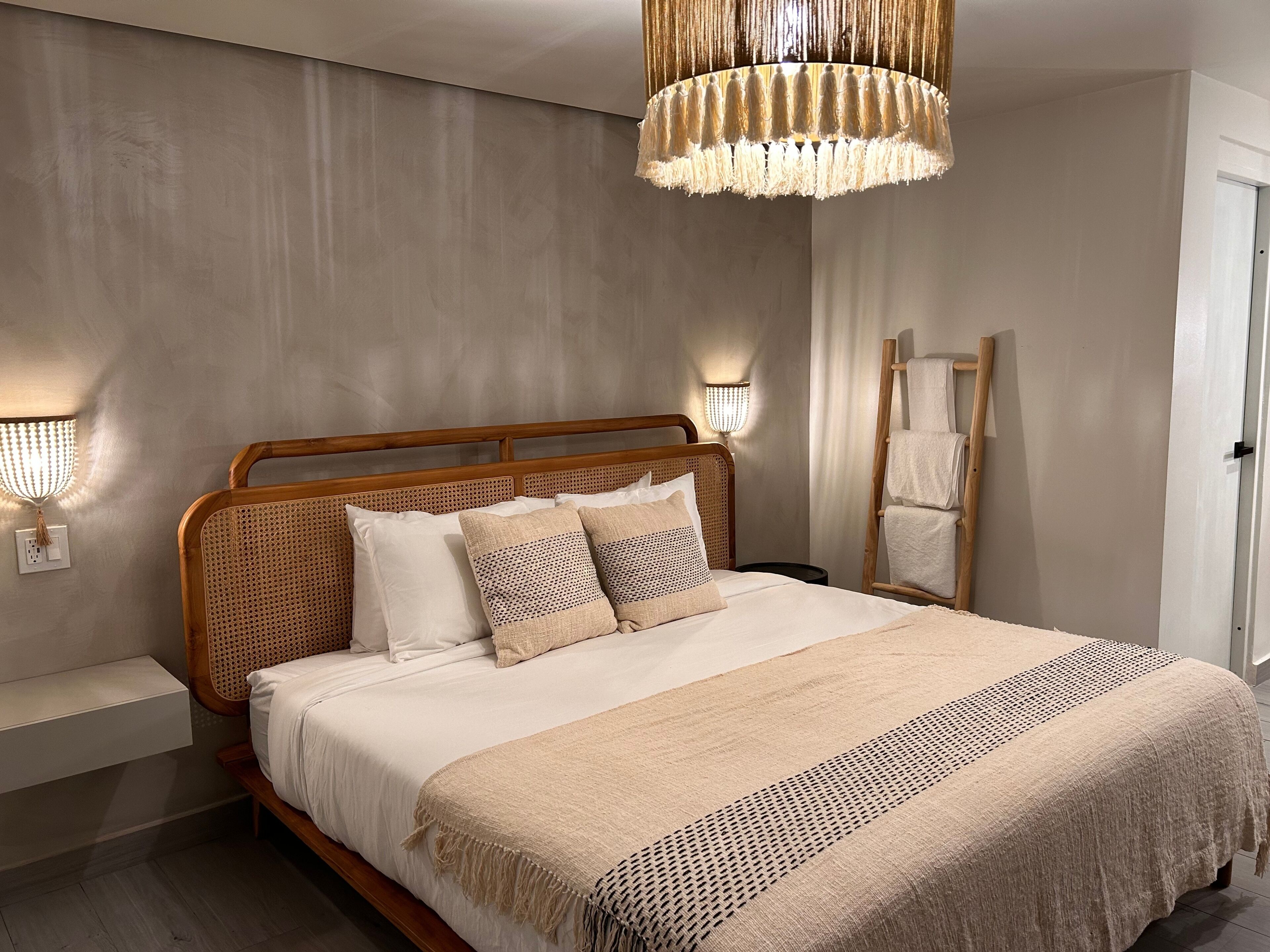 Un dormitorio con estructura de cama de madera, ropa de cama blanca y una manta tejida.