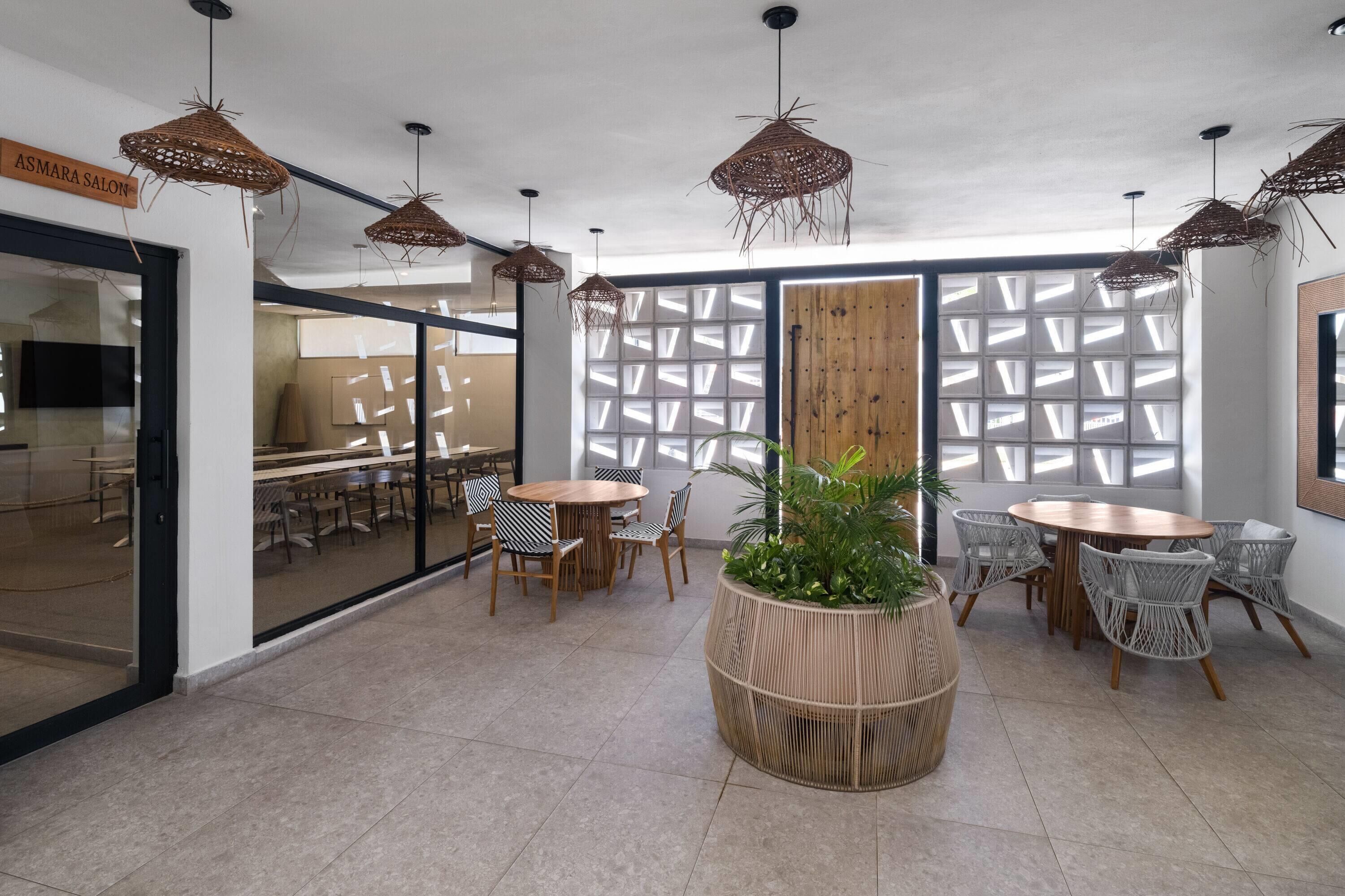 Un interior moderno con lámparas colgantes de mimbre, una planta central y una combinación de mesas redondas y cuadradas con sillas de mimbre.