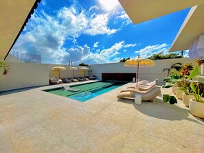 A modern outdoor pool area with lounge chairs and umbrellas, surrounded by potted plants and a clear blue sky. - Bali Hotel Adults Only Isla Verde, a Trademark by Wyndham (Carolina)