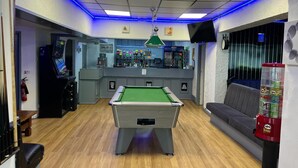 A pool table in a room with a bar area, a sofa, and a gaming machine. - Henson Hotel (Blackpool)