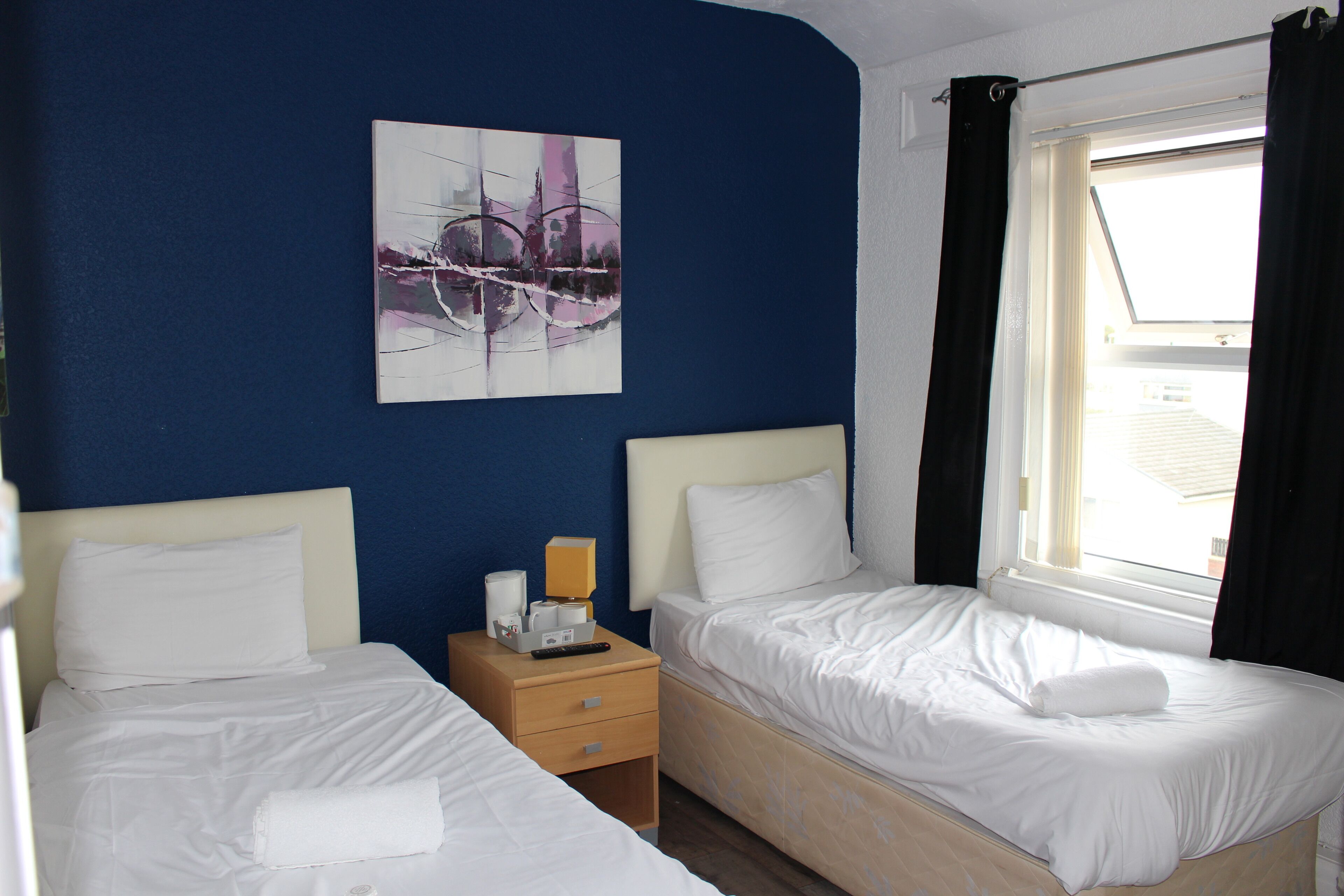 A hotel room with two beds, a nightstand with a lamp, and a painting on the wall.