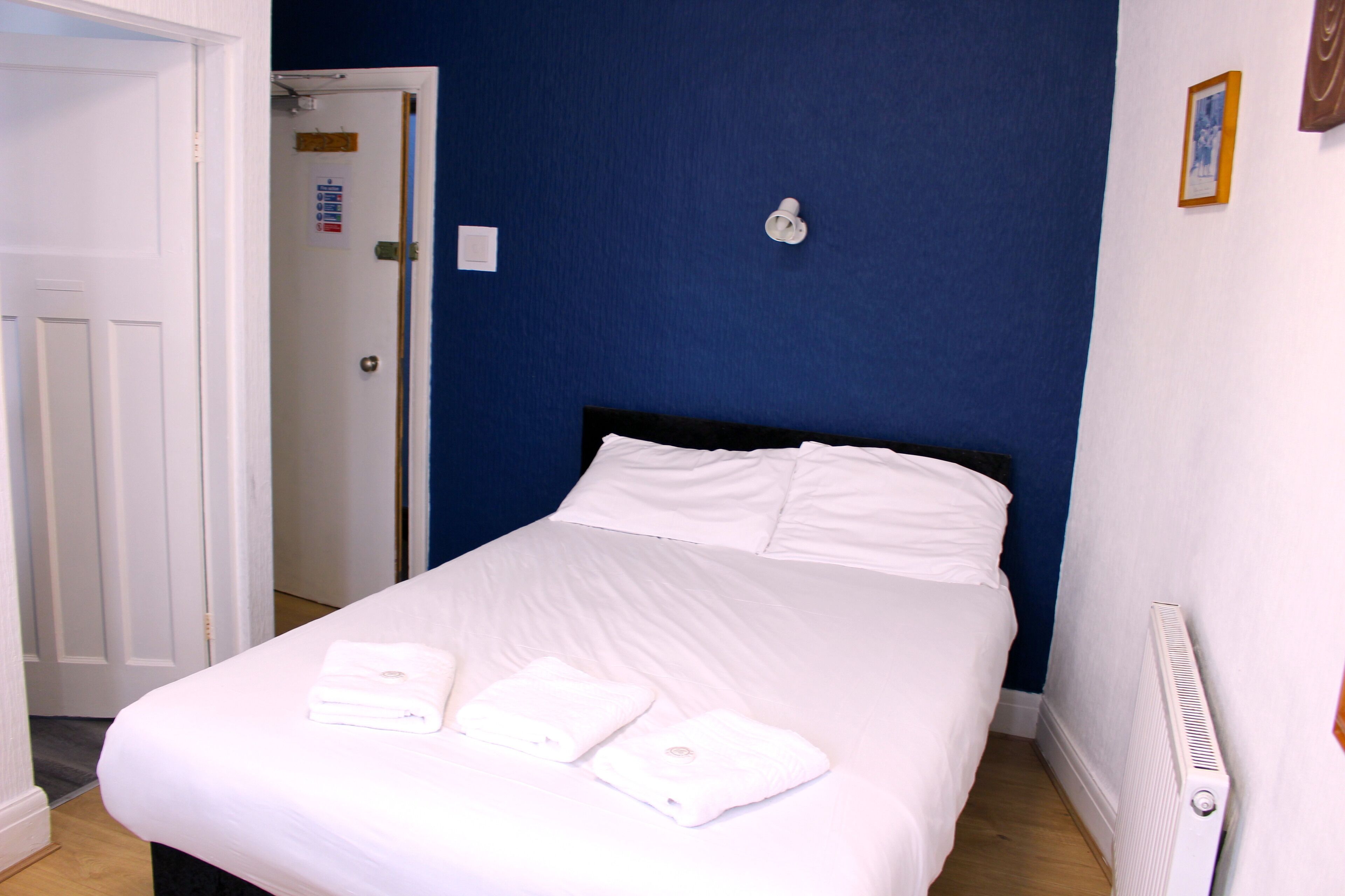 A neatly made bed with white linens and two towels, a white door, and a blue wall.
