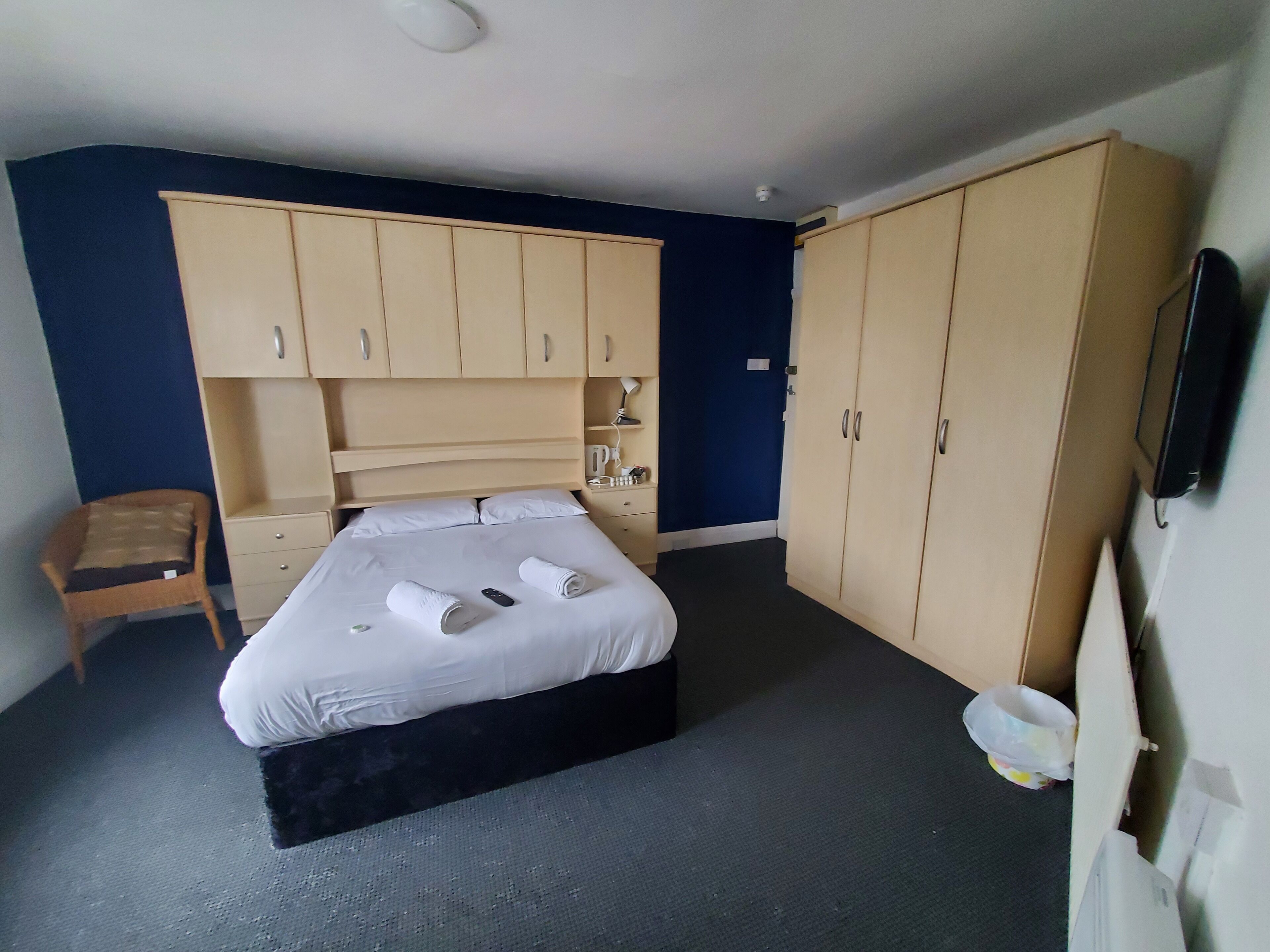 A hotel room with a bed, a chair, a wardrobe, and a television.