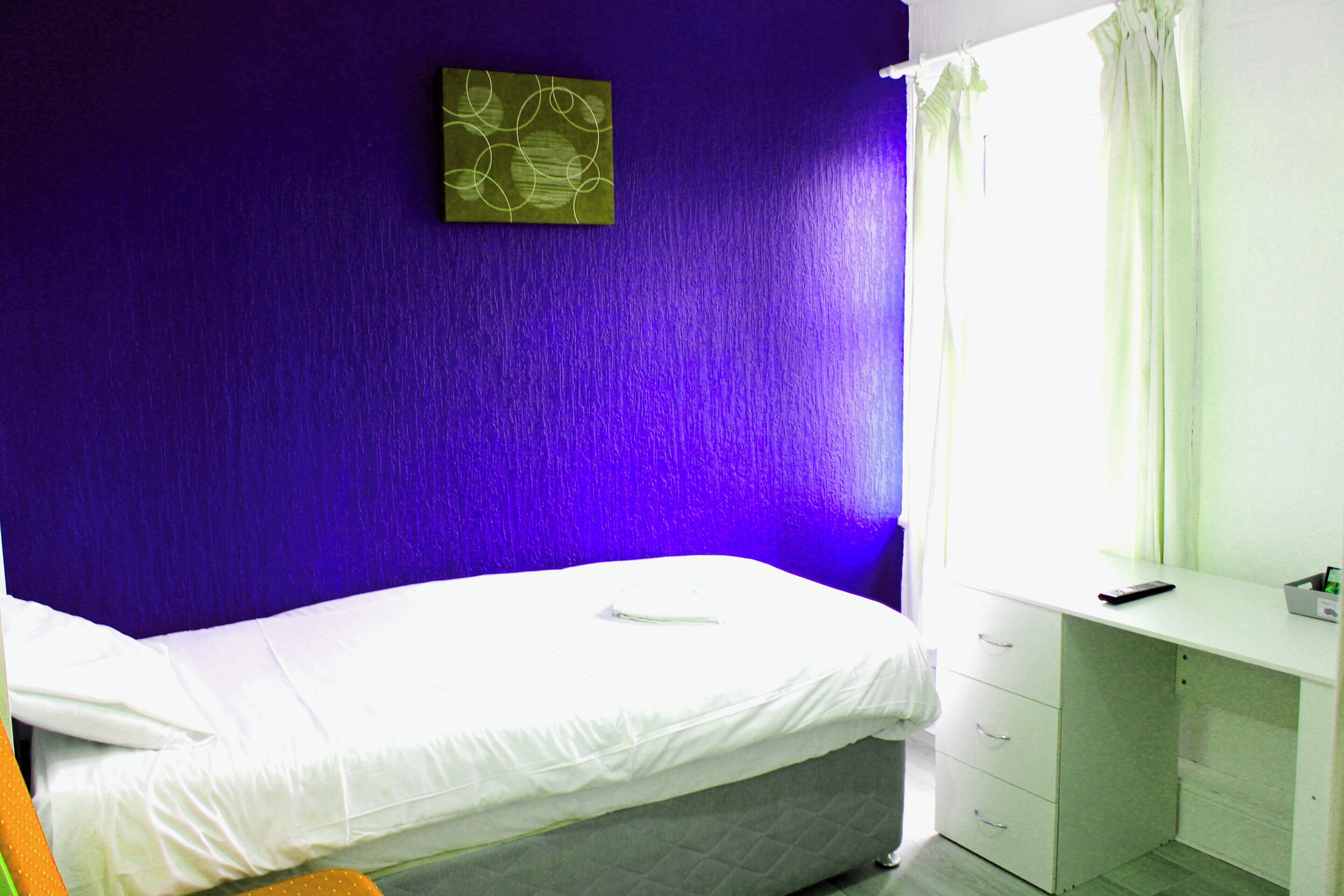 A room with a bed, a desk, and a window with curtains.
