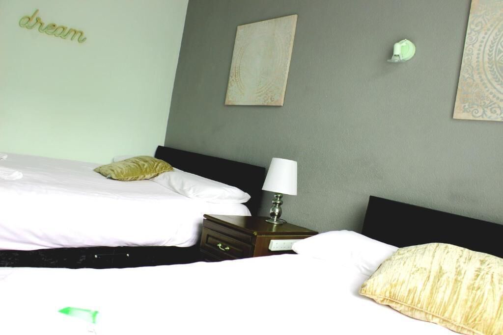 A hotel room with two beds, a nightstand with a lamp, and artwork on the walls.
