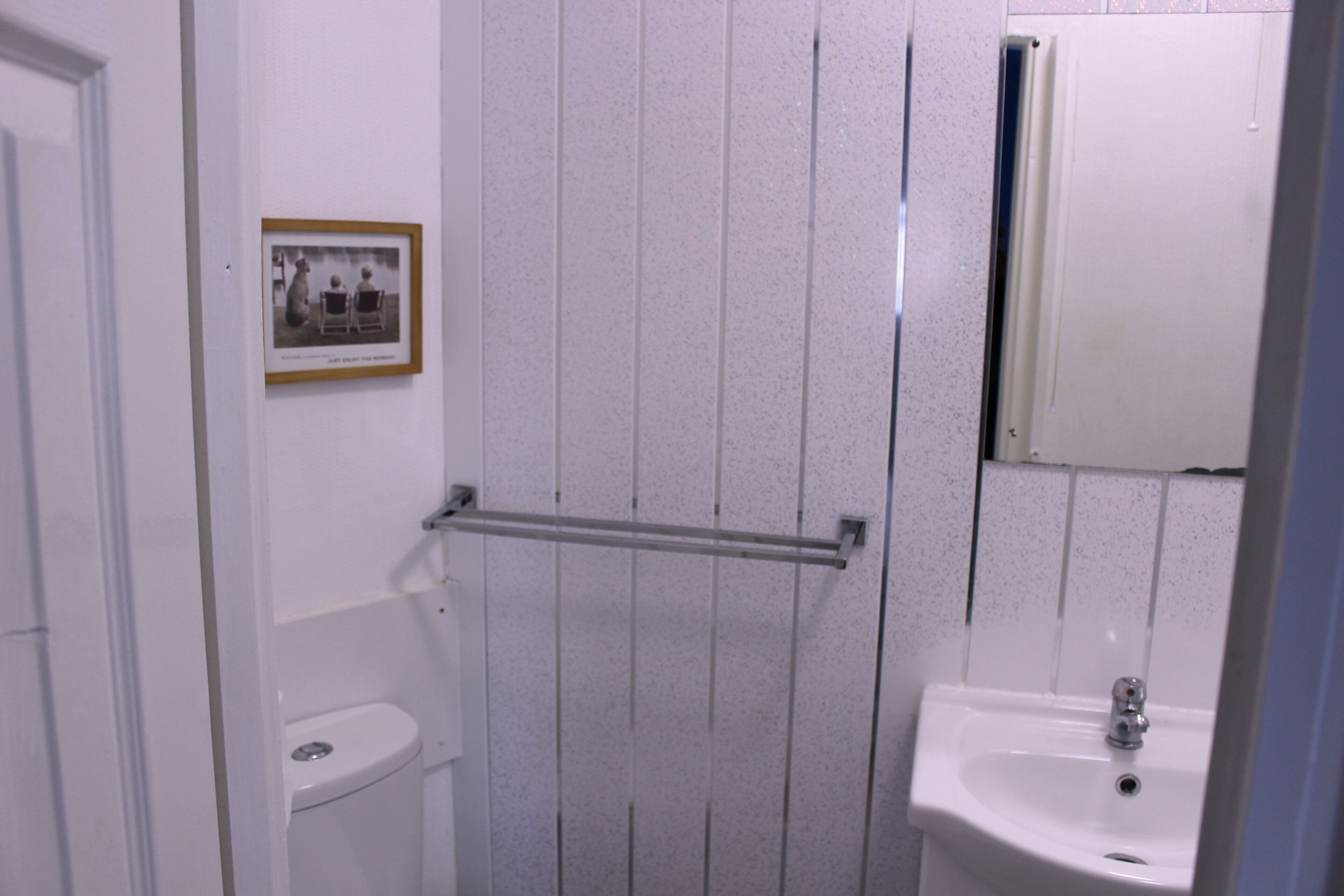 A bathroom with a toilet, a sink, a towel rack, and a framed photograph on the wall.