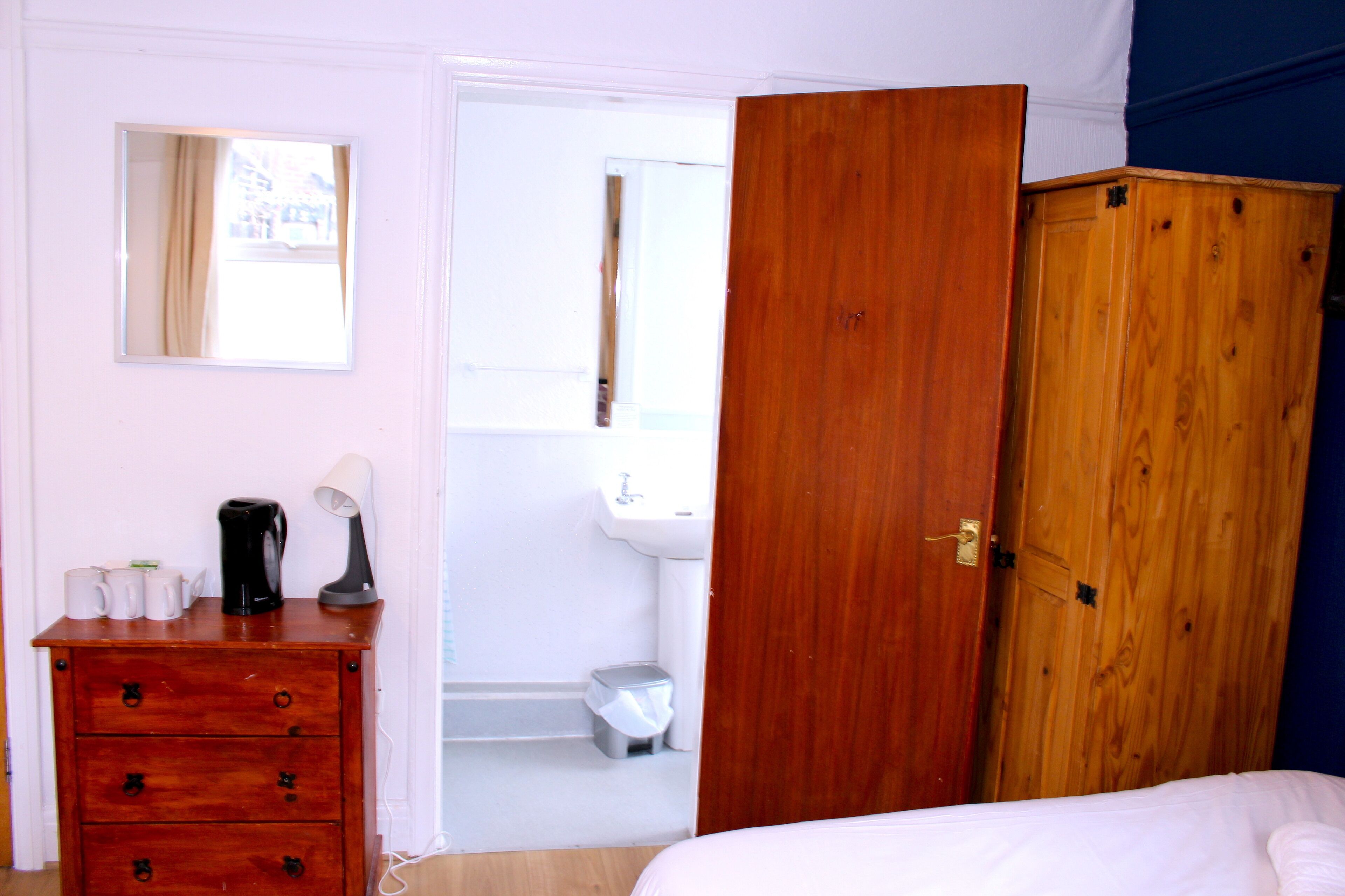 Une chambre avec une armoire en bois, une table de chevet avec une lampe, et une vue sur la salle de bain.