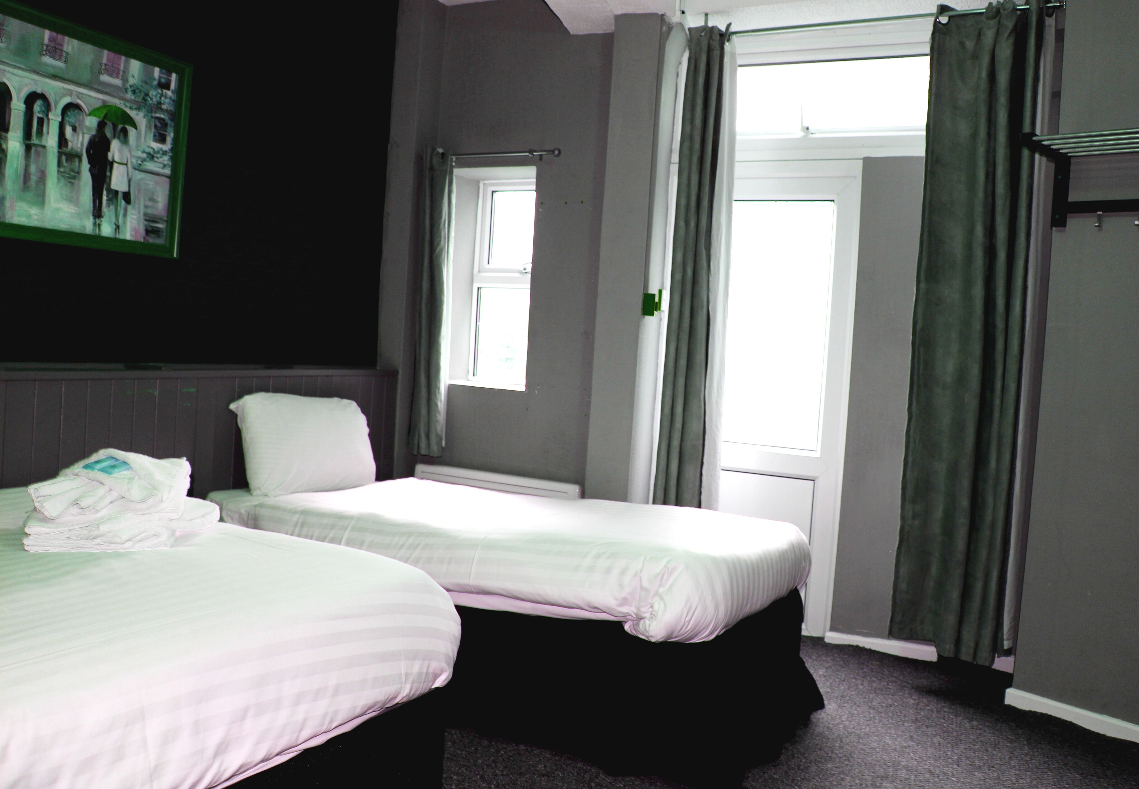A hotel room with two beds, a window, and a painting on the wall.