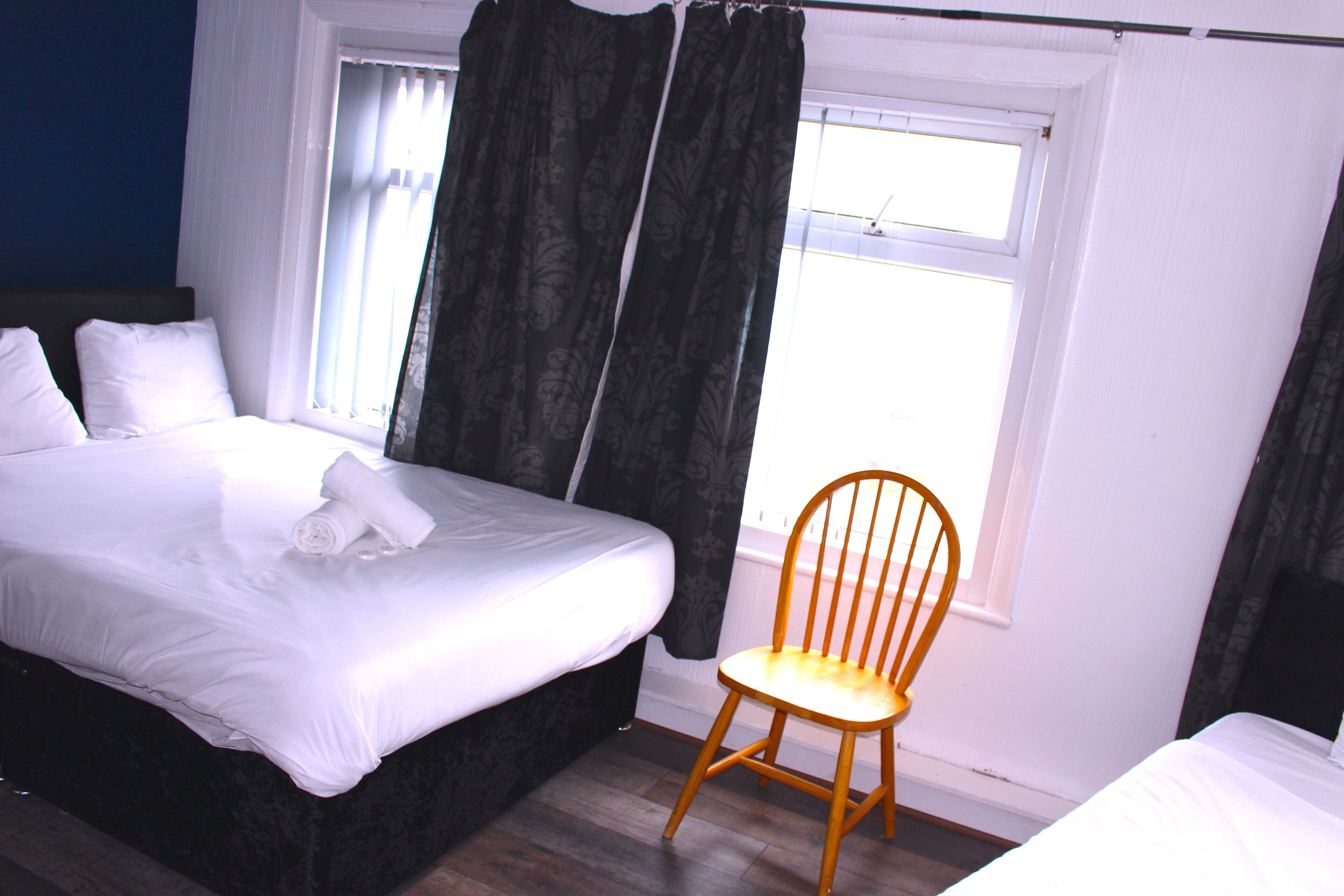 A hotel room with a bed, a wooden chair, and a window with curtains.