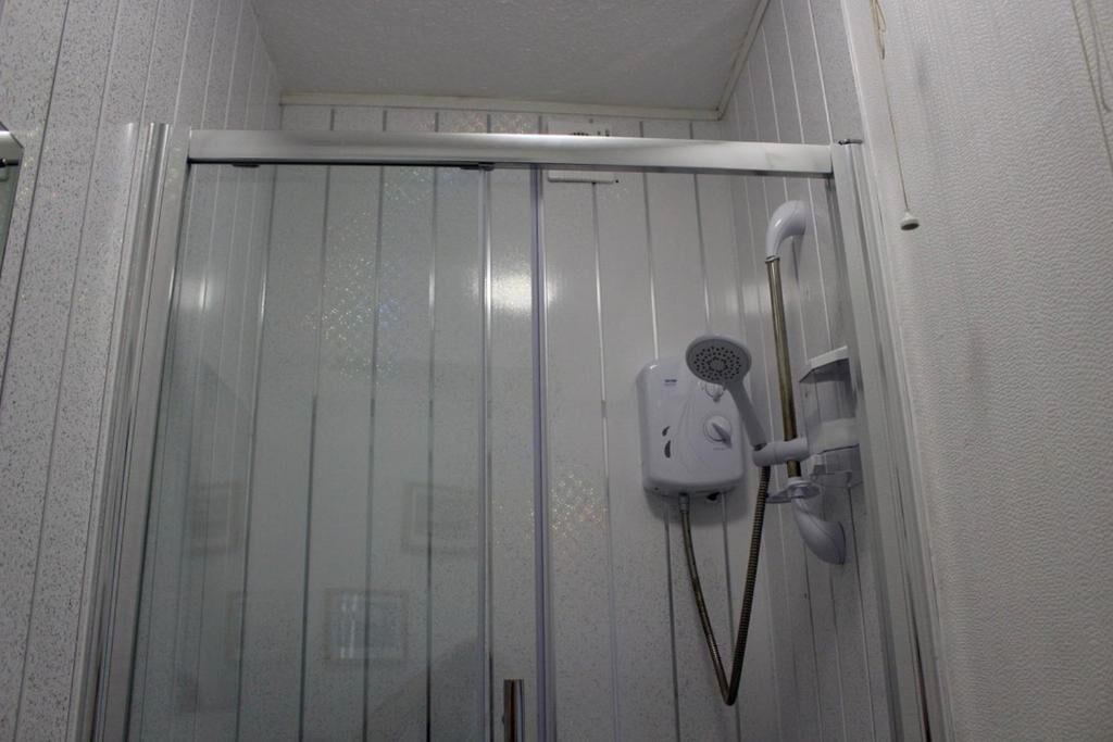 Chuveiro com porta de vidro, chuveiro manual e torneira fixada na parede.