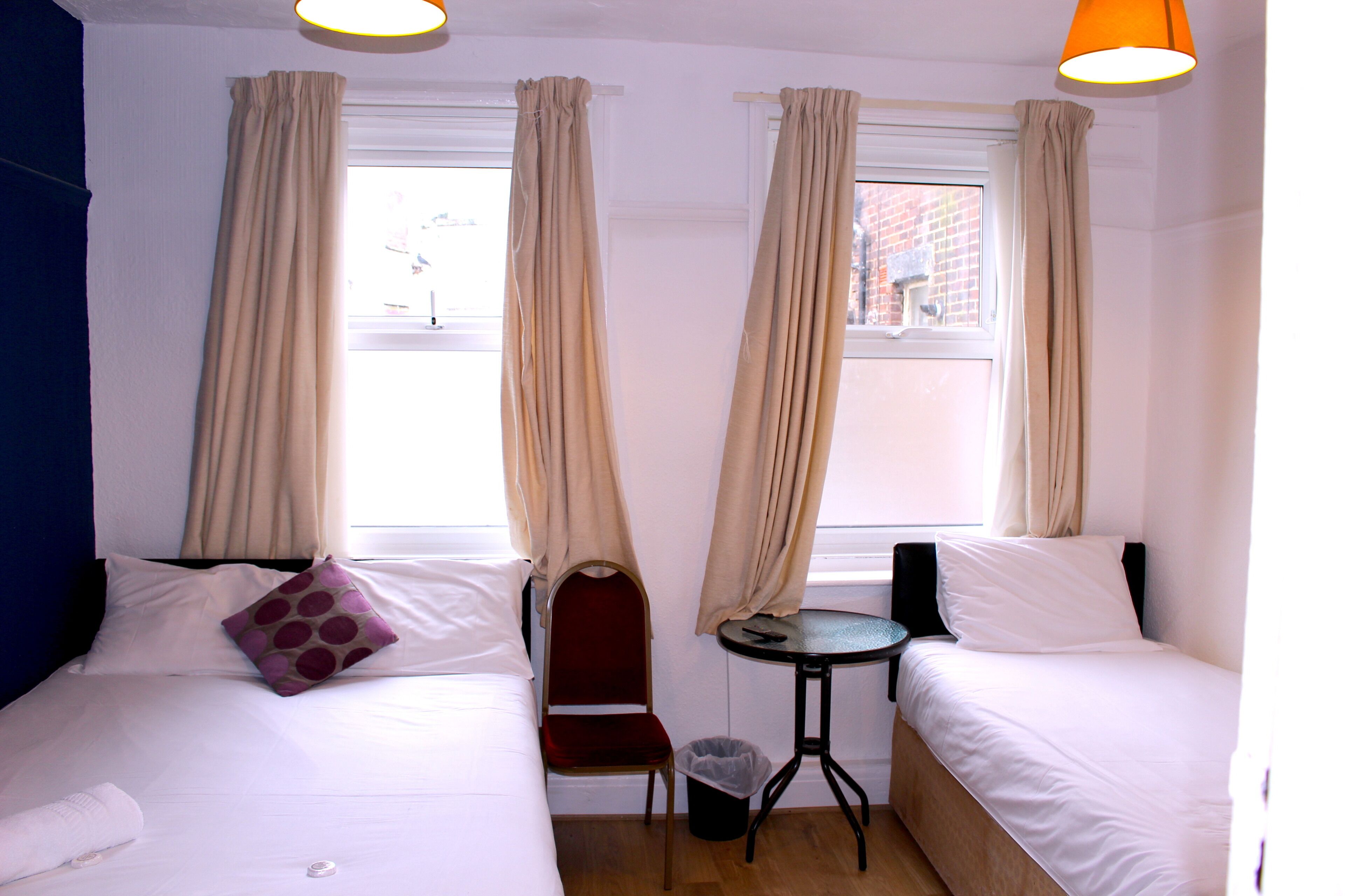 Une chambre d’hôtel avec deux lits, une petite table, une chaise et une fenêtre avec des rideaux.