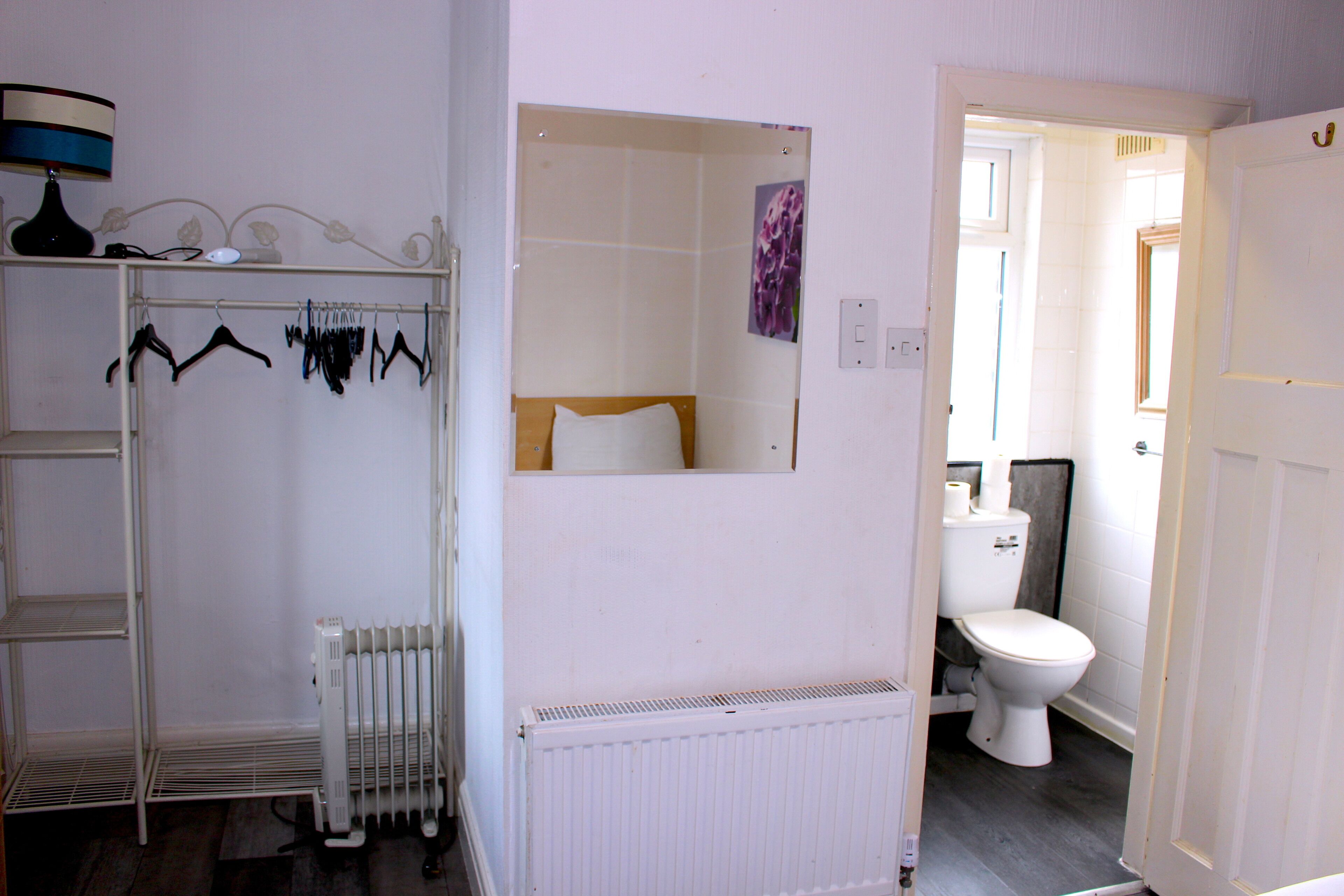 Een badkamer met een witte radiator, toilet en spiegel.