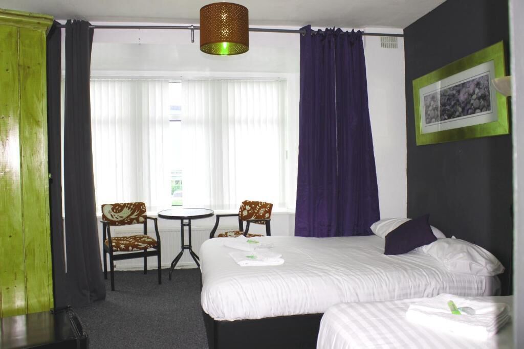 Une chambre d’hôtel avec un lit, deux chaises, une petite table et une fenêtre avec des rideaux.