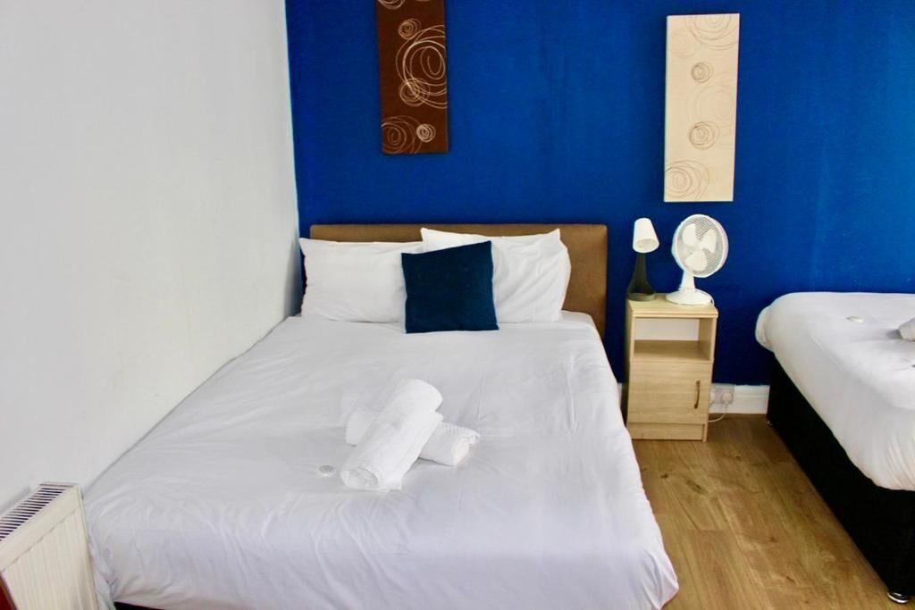 Een hotelkamer met een groot bed, twee nachtkastjes en een kleine ventilator.