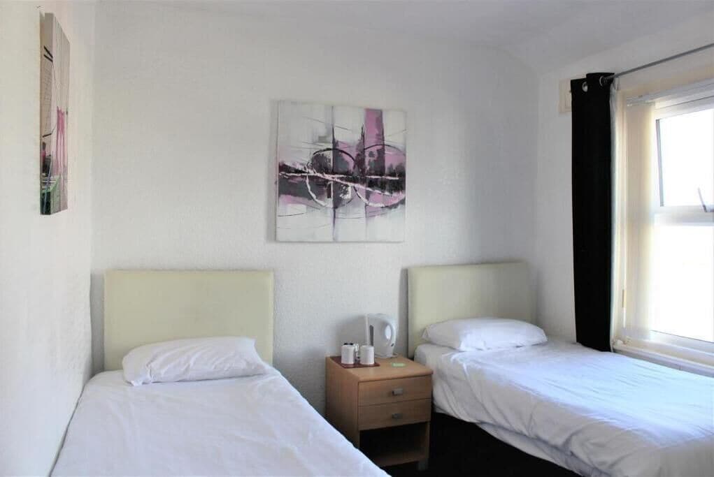 A hotel room with two single beds, a nightstand with a lamp, and a painting on the wall.