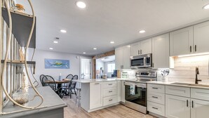 A modern kitchen with white cabinets, stainless steel appliances, and a wooden dining area. - private beach,gated parking,showers bathrooms (Myrtle Beach)