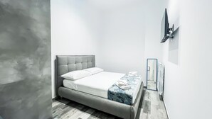 Une chambre moderne avec un lit, un luminaire au plafond et un téléviseur fixé au mur.