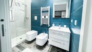 Une salle de bain moderne dotée d’une douche à parois de verre, de toilettes blanches, d’un bidet et d’un meuble-lavabo avec un miroir.