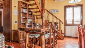 A wooden staircase with a spiral design leading to a dining area with a large wooden table and chairs. - Appartamento Panoramico Edolo (Vico)
