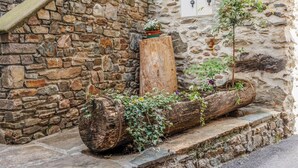 A rustic stone wall with a wooden log planter filled with greenery and flowers. - Appartamento Panoramico Edolo (Vico)