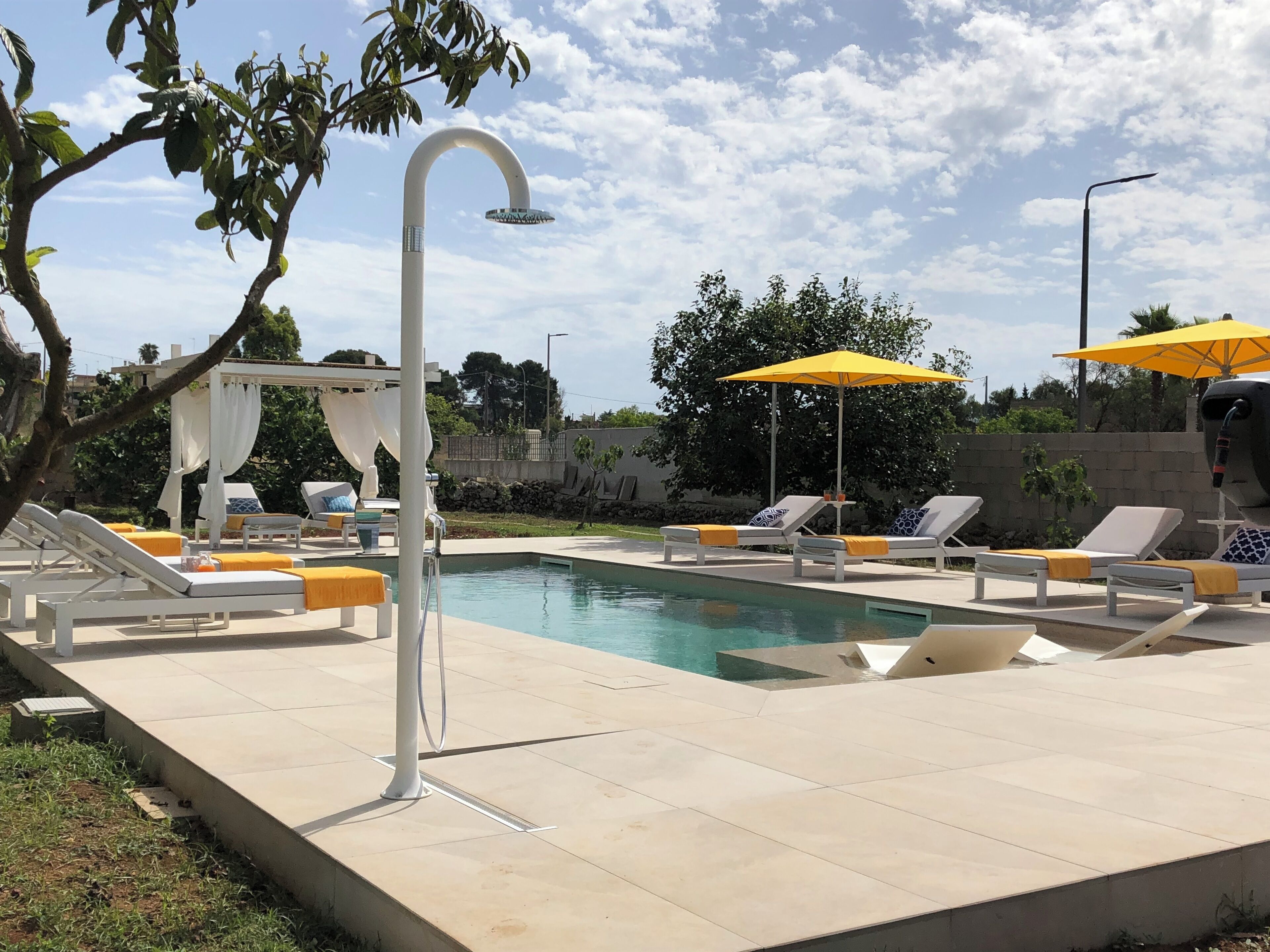 A pool area with lounge chairs and umbrellas, a white pergola, and a clear sky.