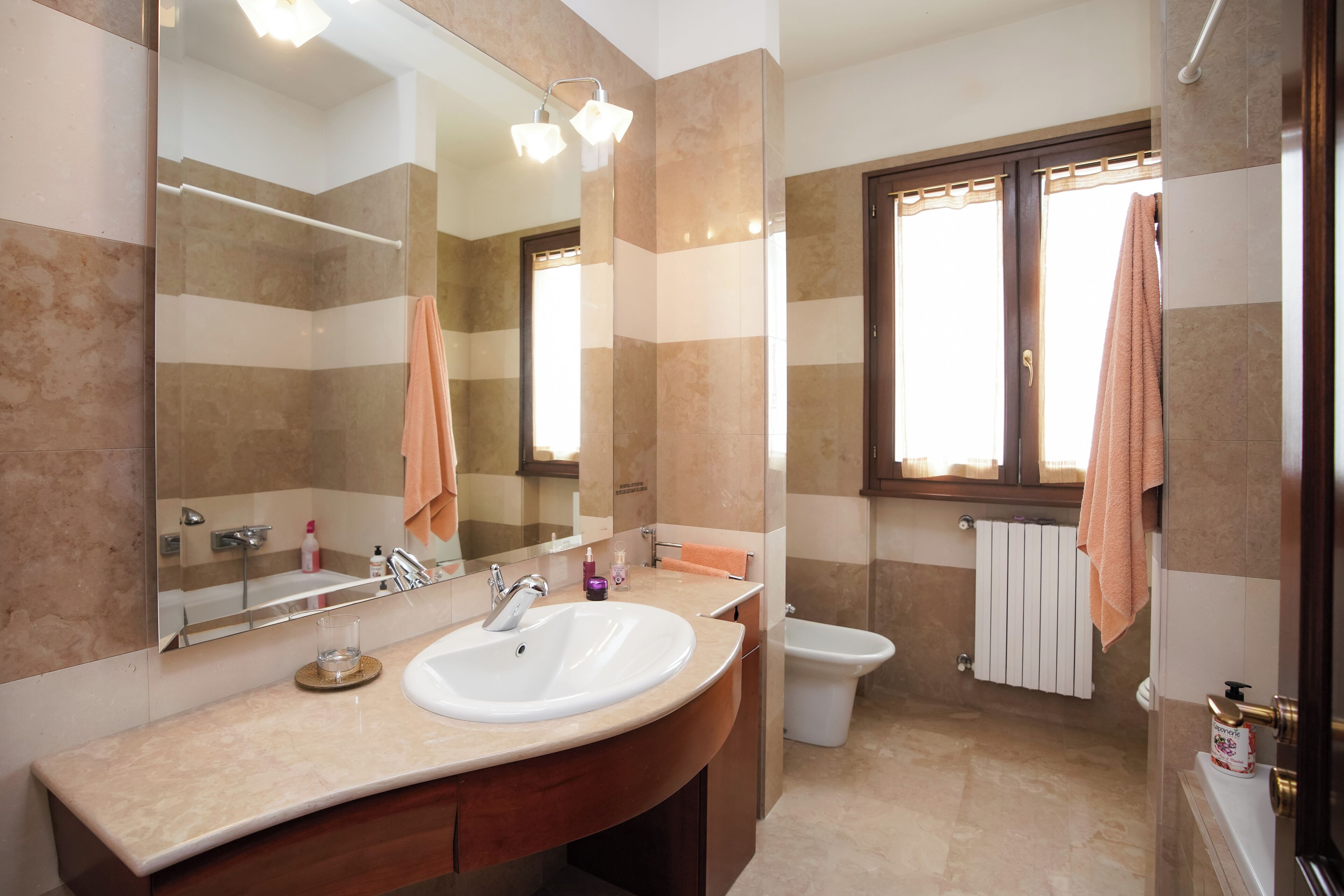 Een badkamer met een grote spiegel, een wastafel, een toilet en een raam, met een handdoek aan de deur.