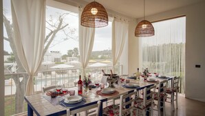 A dining area with a table set for four, white chairs with floral upholstery, and two woven pendant lights. -  Beautiful villa with pool in Specchia (Specchia)