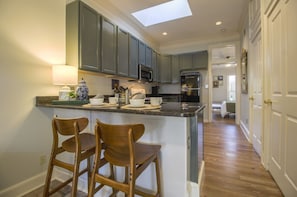 A kitchen with a skylight, dark cabinets, a microwave, and a refrigerator. There are two wooden chairs at the counter.