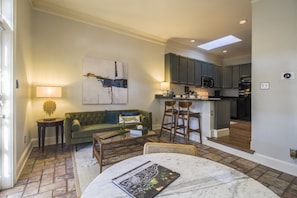 A living room with a sofa, coffee table, and a dining area with a table and chairs. There is a kitchen area with cabinets and appliances.