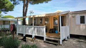 A mobile home with a porch, a fenced area, and a tree. - Mobil-home au Camping 4 Étoiles Familial Les Sables D'or (Agde)