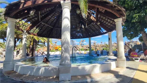 A covered pool area with a central water feature, palm trees, and a tropical setting. - Mobil-home au Camping 4 Étoiles Familial Les Sables D'or (Agde)