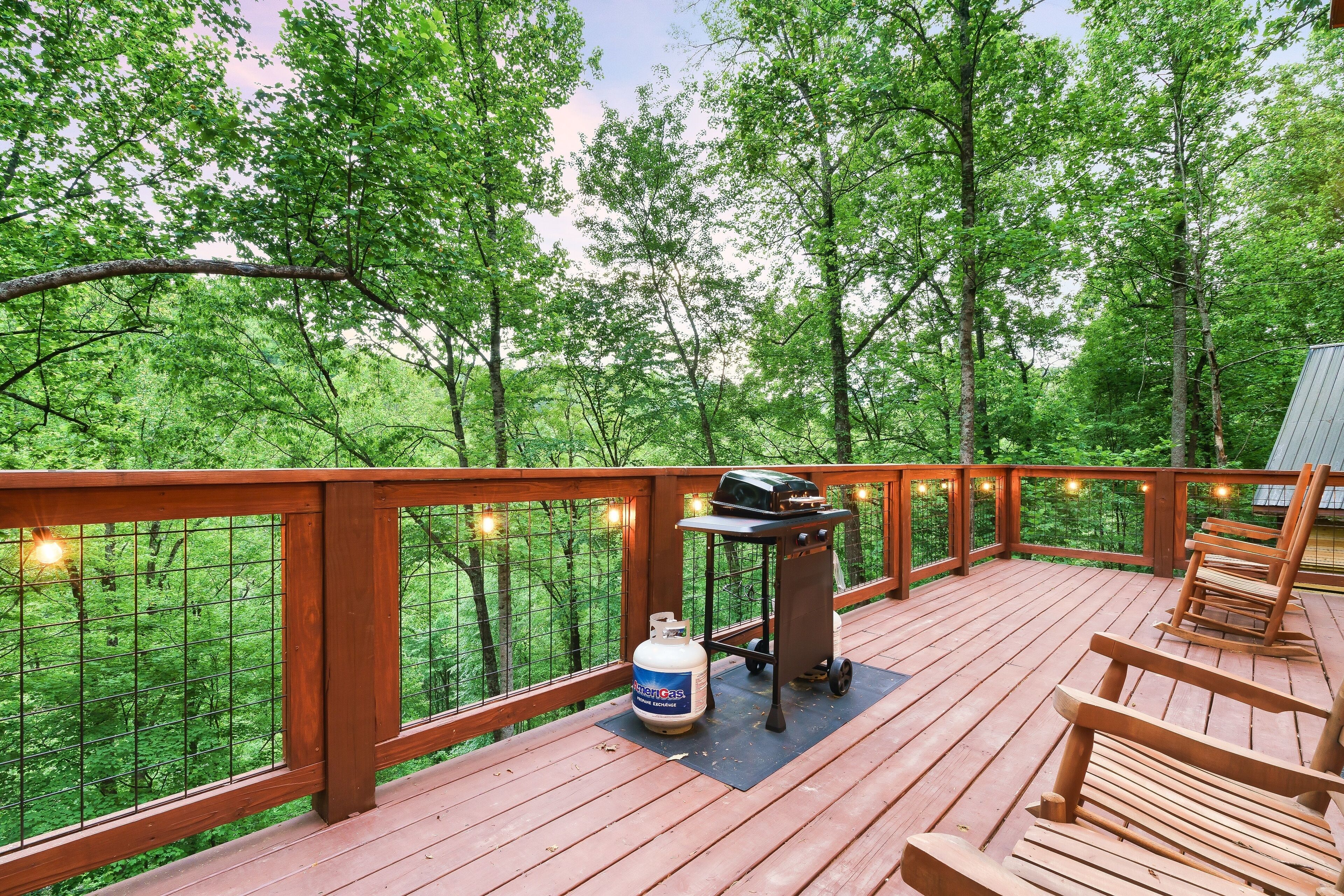 A wooden deck with a grill and propane tank, surrounded by a wooden railing and string lights.