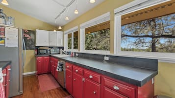 Una cocina con armarios rojos, encimera negra y ventana con vistas a árboles.