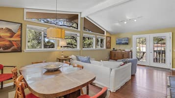 Amplia sala de estar con una mesa de comedor de madera, un sofá blanco y un ventanal con vista a árboles.