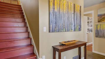 Una escalera con acabado de madera, un cuadro colgado en la pared con un paisaje de árboles y una pequeña mesa de madera con un cuenco.