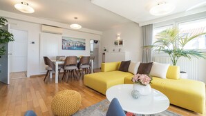 Ein modernes Wohnzimmer mit einem gelben Sofa, einem Essbereich mit Stühlen und einem weißen Couchtisch.