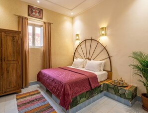 Un dormitorio con una cama grande, un armario de madera, un ventanal con cortinas, una lámpara de pared y una planta en maceta.