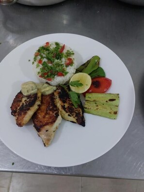 A plate with grilled chicken, rice topped with a green herb mixture, grilled vegetables, and a slice of lime. - Hllol Hotel Abu Simbel (Abu Simbel)