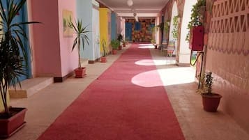 Corredor de hotel com carpete vermelho, plantas em vasos e paredes coloridas.