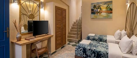 A hotel room with a desk, a television, a bed with patterned bedding, a painting on the wall, and a staircase.