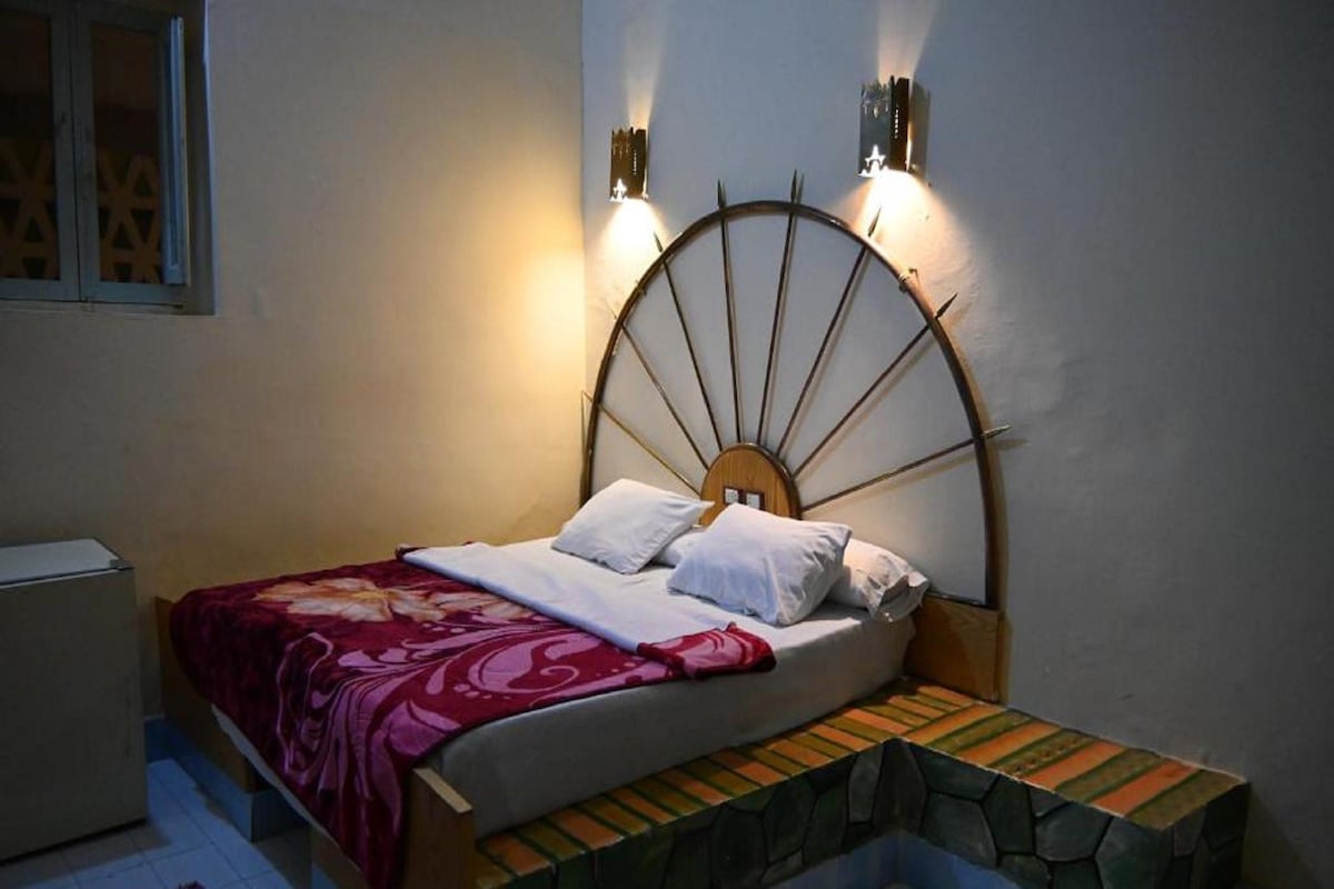 A bed with a unique headboard, a bedside table, and a small bench at the foot of the bed.