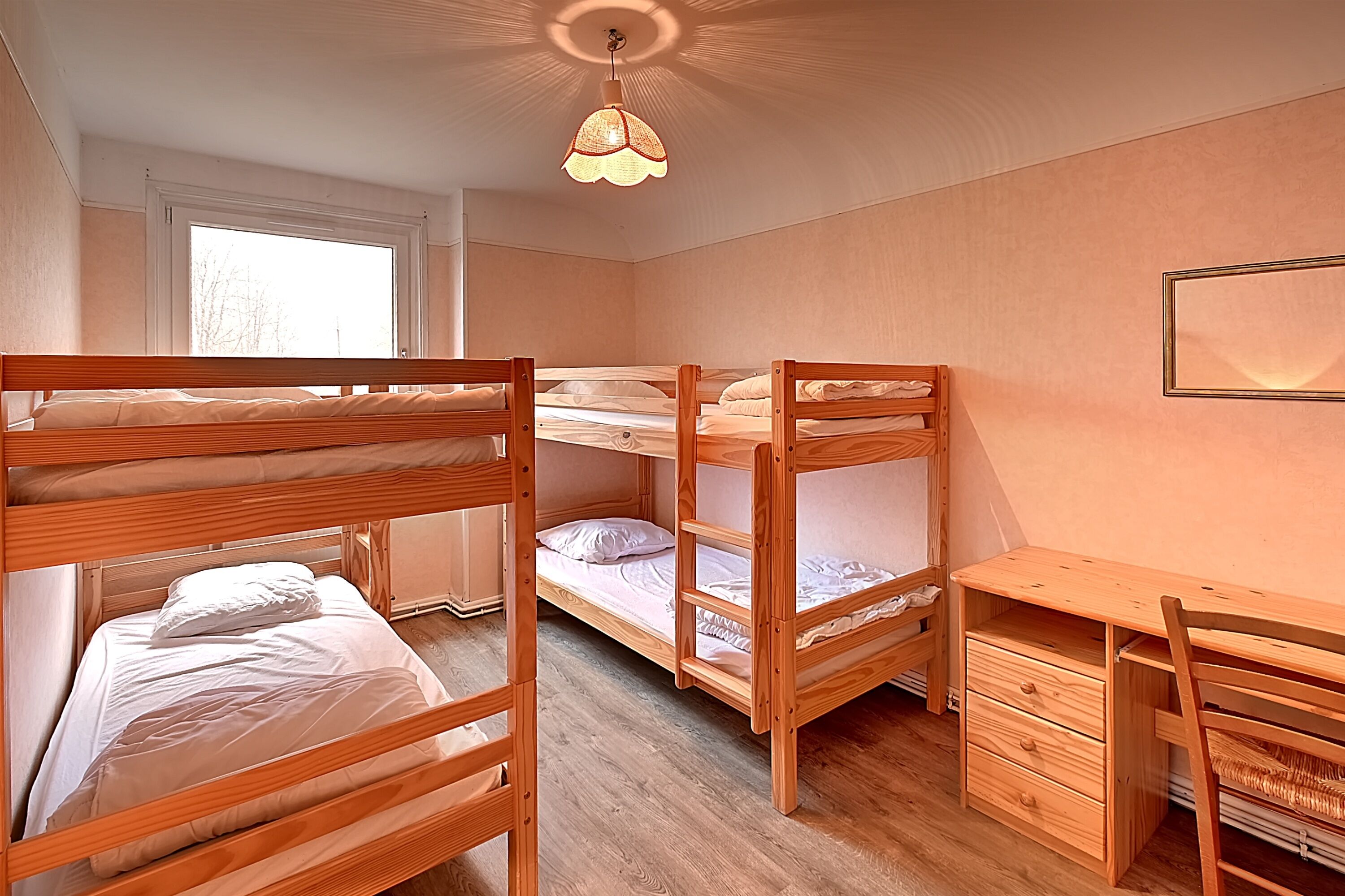 A bunk bed room with a desk and a hanging light fixture.